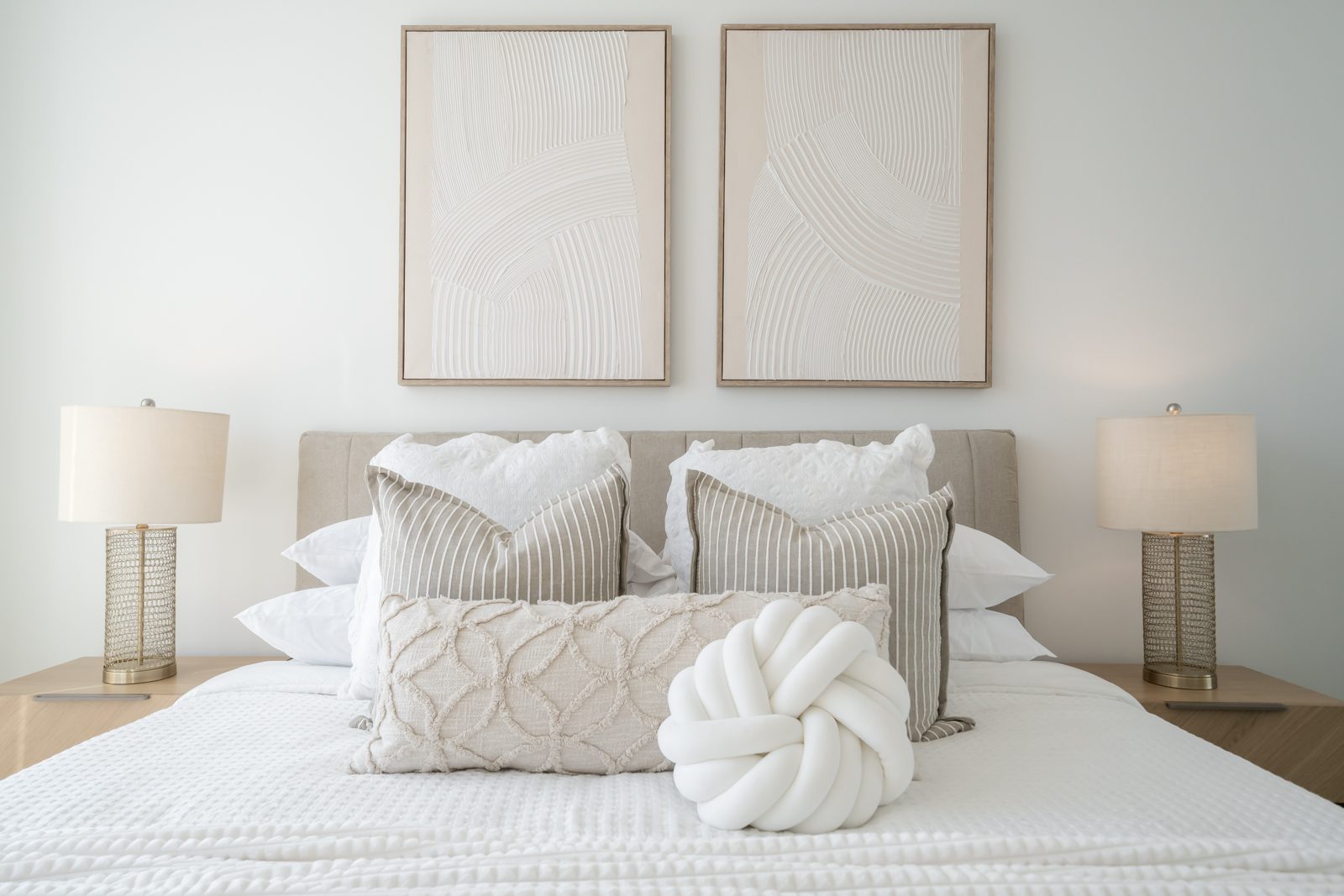 Bed with layered neutral pillows and textured art